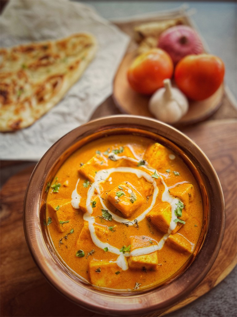 paneer butter masala in a serving bowl with a naan on the side